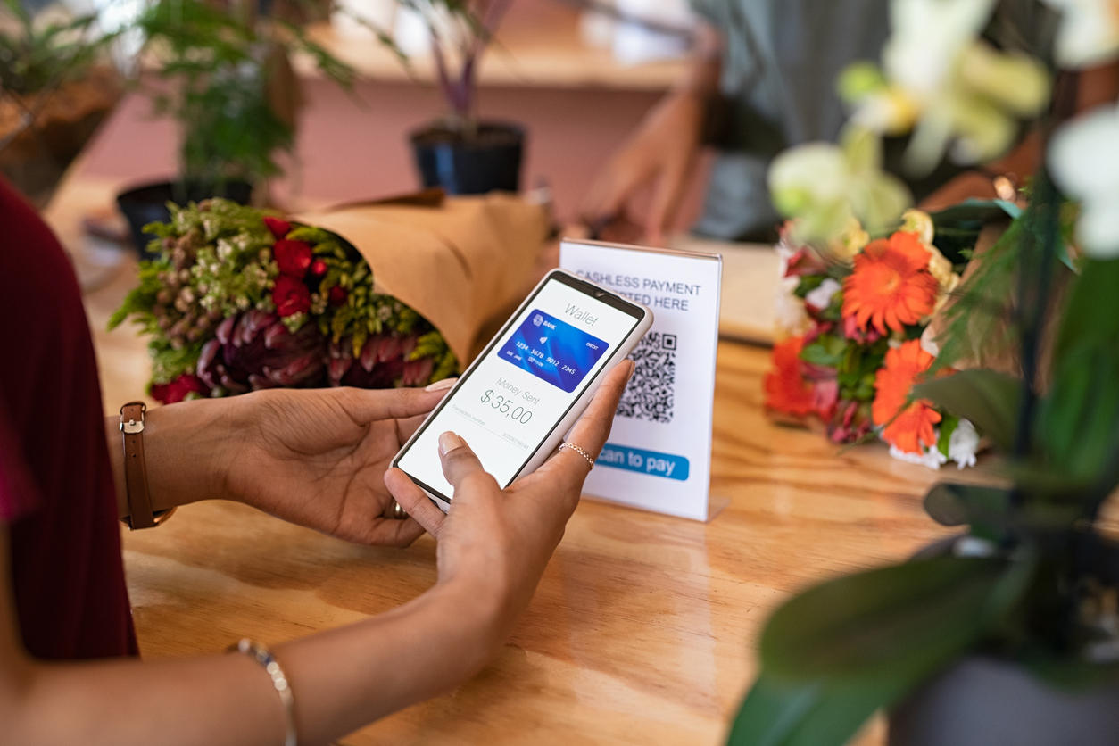 Close up of woman hands holding smartphone scanning QR code while paying florist. Latin young woman paying cashless money using smartphone after buying fresh flowers. Customer hand making payment through smart phone app in store that accept digital payments - The Mobile Payments Revolution